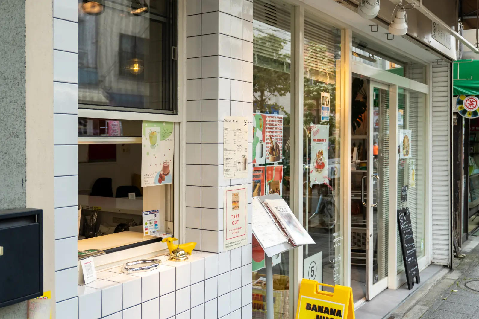 商店街に面した店の外観。白いタイルのテイクアウト窓と黄色の立て看板